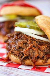 A close-up view of a slow-cooker BBQ brisket sandwich with a sliced onion and pickles on a checkered cloth.