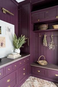 Purple mudroom design features an aubergine and purple stone bench under aubergine shiplap trim, aubergine mudroom cabinets accented with brass hardware and red brick herringbone pavers.