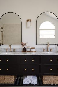 The Black Everett 72 Inch Oak Double Sink Bathroom Vanity with a White Carrera Marble Top paired with brass hardware dazzles in this luxurious bathroom design from @homewithjanny below alluring arched mirrors. The look is timeless!