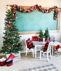 A large green chalkboard sits above a white and gray table with matching chairs in this neutral playroom. Christmas decor such as a rag tie garland, red buffalo plaid cushions, and a decorated tree surround the space on a beige carpet...   Image: a.firemans.wife