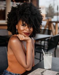 Woman outside with short coily hair drinking water