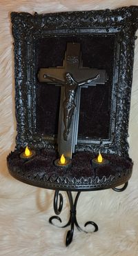 Whether you are a devout follower, a religious artwork fan or simply like black home decor,  look no further.  This piece gives the owner a choice of crucifix placement (we're big St. Peter crucifix fans here) and a spot for the electric/battery operated tea lights that it comes with or add your own candles to it (careful! It's not flame retardant). The faux moss is black with hints of burgundy, giving it a type of visual illusion of movement. It measures 22" tall, 12.5" wide and sits 6.75" off