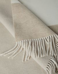 Cashmere double cloth throw with border and fringe Thanks to special workmanship that involves numerous steps and precise finishes, this double cashmere throw offers a warm, even and light texture, providing a nice and cozy sensation. The main side showcases a contrast color band on the edge, while the reverse side is designed with a third color to create a sophisticated combination in the iconic neutral colors of the Brunello Cucinelli collections.