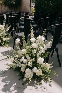 White and black for white wedding colors 2025, black bridesmaid dresses, white bridal gown, dark blue groom suit and white flower boutonniere, white flowers and greenery of bouquets, centerpieces and wedding aisle chairs décor, black wedding napkins, white wedding cake with black ribbons, black and white wedding invitation suite.