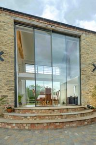 These tall glass doors fill the doorway of an old threshing barn door. The double height glass doors are sliding with a slim frame to maximise light into the existing threshing barn doorway. Click on the image to see more pictures of these tall glass doors. 