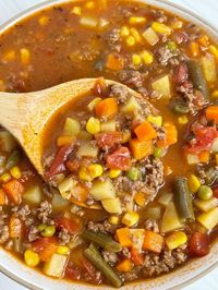 A white bowl with hamburger soup in it and a wooden spoon with some on it.