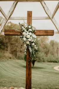 White green arrangement placed in the center of a wooden cross. Wedding ceremony aisle landscape aesthetic rustic