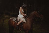 Country bride horse riding in her gathered up wedding dress. Photographed by @ barefootandbearded. This raw & wild bride is rocking the Calloway Ash hat on her special day!