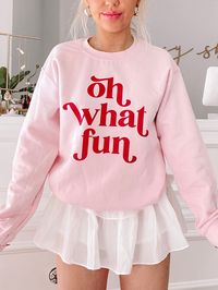 Our Oh What Fun Crewneck is a light pink crew neck with a soft fleece lining on the inside of the sweatshirt. "Oh What Fun" is written in red on the front side. fit : True to size, model wearing a size small