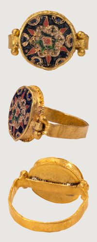 BYZANTINE CLOISONNÉ RING. Constantinople?, 10th century, gold, enamel, bezel 13 x 14 mm. This ring has been reassembled in modern times by joining a reeded gold band with four gold granules to a circular flat roundel with floral design in red, blue, green and white cloisonné enamel. The cloisonné medallion is soldered at the junction of the bezel and the hoop, which has been flattened where it passes behind the bezel. Besides some pitting on the enamel surface.