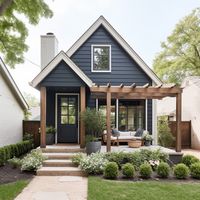 A small, tiny blue farmhouse cottage with blue siding, black windows, and natural oak wood front porch. Design: @windthekey Follow @windthekey for more design inspiration.