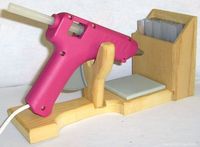 Glue Gun Holder Stand-It made of sturdy wood with a ceramic tile to catch drips. It holds regular and mini glue guns. The attached box holds all size glue sticks, scissors, and other craft tools. It measures 11" long x 3 1/2" wide x 5 1/4" high box.