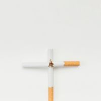 Cross sign made from broken cigarette over white background