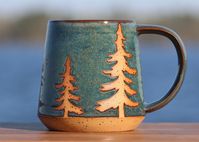 The speckled clay silhouette of two evergreen trees are highlighted behind a northern light sky.  Each mug is dipped in our handmade, non-toxic glaze, exposing the fired speckled brownstone clay. Our handmade Offshore Blue glaze has deep shades of blue, gray, and green. The wide handle is a perfect fit while enjoying your favorite hot beverage. Microwave and dishwasher safe Capacity is approximately 14 ounces Dimensions: approximately 4 inches tall and 3.25 inches in diameter We do our best to a