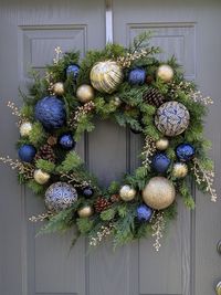 This is a gem of a wreath showcasing ornaments in Saphire blue and shimmering gold.  This wreath would make quite the statement on your front door for the Holidays.  The beauty can be brought inside to show off a room, or it would make an excellent Christmas gift. This wreath is made on a round metal wreath form with faux evergreens and adorn with shatterproof dark blue and gold ornaments.  Secured with wire and hot glue. Overall size with ornaments and greenery 27x26x6 1/2.  Best on a covered p