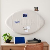 Hey, baller! Put your love of the game on display with this football-shaped pinboard. A sturdy design, this decor is subtly cushioned and covered in linen, creating an all-star spot for notes, pics and mementos. Made of EPS and linen, MDF (medium density fiberboard), EVA and linen. Keyhole mounting hardware included; 2 anchors and 2 screws. Includes 20 push pins. Imported.