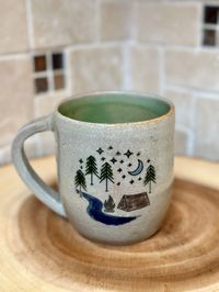 Handmade Colorful Outdoor Mug with Handle -Ceramic Pottery is food, dishwasher and microwave safe -Glazed with Off-white background (variations in glaze are normal and make this piece unique) -Decorated on both sides with a colorful outdoor scene. one side featuring a camping scene next to a vibrant blue river. the other side features various trees in greens with the rising sun.  - The interior is glazed in a light green .  -Cup/Mug is 4" W x 3 1/2" H. Width including the handle is 5" -Holds 14oz of liquid, great for big cup of coffee or tea! Art is my zen. In the many forms it takes, art helps me meditate, de-stress and take a breather from the moving world.  I am not a "master" of any specific art form. But, I have put my love and time into each piece. So, expect imperfections that give