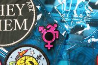 A 1.5 inch soft enamel pin of the Queercrip symbol designed by Sky! Digital drawing by Yuna Baek it featured the new accessibility icon mishmashed with the trans symbol! The symbol is in hot pink glitter with a black background and there are two pin backs with rubber stoppers.