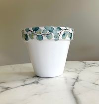 Eucalyptus clay pot. A beautiful addition to a sunroom and a great gift idea!  Does have a drainage hole, the pot measures 6 inches high and 6.5-inch diameter (top). This pot is hand painted white, and the design is a decoupage technique.  The lovely eucalyptus design is wrapped around the entire pot. This is a clay pot, so please use a plastic liner/nursery pot if planting a live plant and keep the pot indoors to protect the design. This planter is a great addition to any boho or neutral themed decor! It adds a simple touch of elegance to any room. *Plant not included.