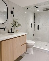 A basement bathroom with no windows therefore no natural light. We chose white polished calacatta tile to reflect any light from the main space, and white counters to keep it open and airy. High contrast woth black accents and a wood custom vanity to warm things up!