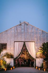 Greenhouse wedding reception with romantic lighting. Outdoor wedding. Floral design with eucalyptus garlands and protea. Antique vineyard chairs at long feasting, farm tables. Soft color palette. Gold flatware, boho chic decor and table settings. This bea