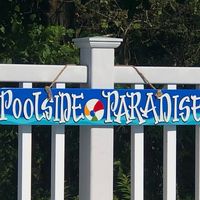 "Poolside Paradise...super fun and bright way to decorate the fence or patio around your pool. This hand painted sign is cypress, which is the wood you want for outside. Exterior paint adds to the durability. The front and back are painted with three coats of exterior paint and then sprayed with a minimum of two coats of enamel. The back is as finished as the front. The sign hangs from a rope and measures 36\"x6\". Check out our other listings for other pool signs. This is real wood. Each piece