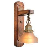 A wall mounted Arts & Crafts style sconce light fixture with a thick wood backplate featuring rounded corners and ebony accents. The lantern hangs from a thick wood arm, has an aged patina finish and a tapered, white glass shade.