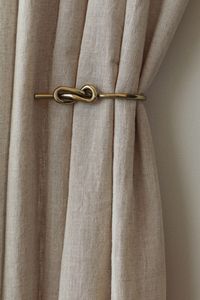 Metal curtain tieback with a decorative knot at front. Predrilled holes for easy hanging. Screws not included. Width 4 in. Length 6 in.