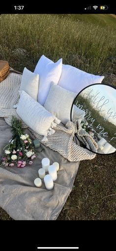 a blanket with flowers and candles on it sitting in the grass next to a mirror