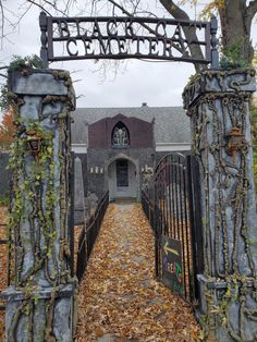 an iron gate with vines and leaves in front of a brick building that says welcome to the cemetery