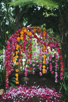 an outdoor wedding ceremony with flowers on the arch and petals all over the ground at the end of the aisle