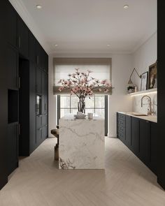 a kitchen with black cabinets and white marble counter tops, along with a vase filled with pink flowers