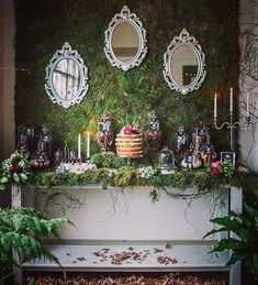 a table topped with a cake covered in greenery and surrounded by mirrors on the wall