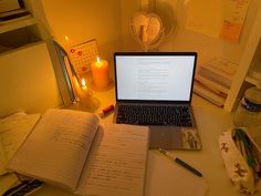 an open laptop computer sitting on top of a desk next to a book and candle