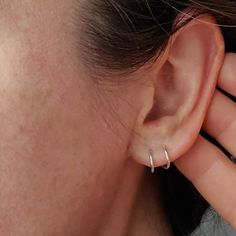 a close up of a person's ear wearing a pair of silver hoop earrings