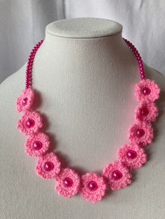 a pink crocheted necklace on a white mannequin with beads and flowers