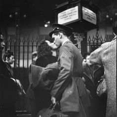 black and white photograph of a man kissing a woman on the street with people in the background