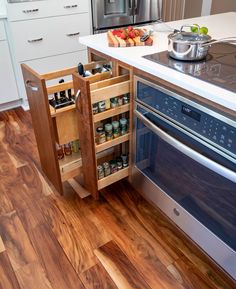 an open cabinet in the middle of a kitchen with wood flooring and stainless steel appliances