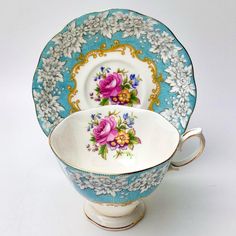 an antique tea cup and saucer decorated with pink flowers on blue, gold trimmings