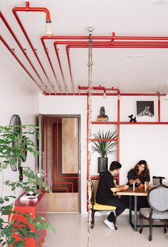 two people sitting at a table in a room with red pipes on the walls and floor