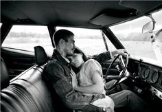 a man and woman sitting in the driver's seat of a car, both holding each other