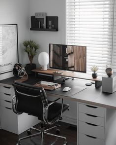 a desk with a monitor, keyboard and headphones on it in front of a window