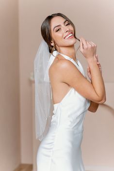 a woman in a white dress is smiling and holding her arm around her neck with a veil over her head