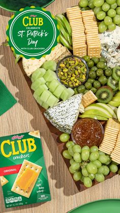 an assortment of cheeses, crackers and grapes on a platter next to a packet of st patrick's day beer