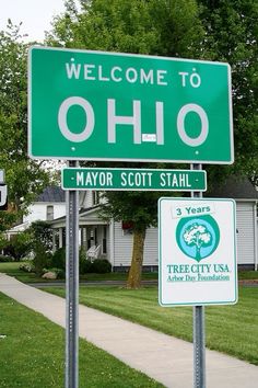 a green street sign sitting on the side of a road next to a lush green field