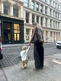 a woman holding the hand of a small child on a sidewalk in front of a building