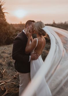 a bride and groom kissing in front of the sun with their veil blowing in the wind