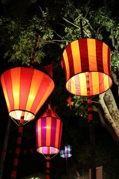 three brightly colored lanterns are lit up in the night sky, with trees behind them