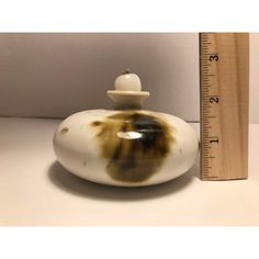 a white vase with brown spots on it next to a measuring tape and a ruler