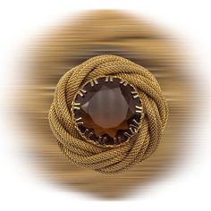 If you love the showy but elegantly made jewelry, this brooch is for you! The beautiful central stone is un-foiled, its topaz brown color is enhanced by the light that passes through it and by the facets It is inserted in a rich golden frame, a twisted effect of the tubular mesh chain  that creates around the stone a comfortable and voluptuous nest where to stay, protected by the decorative prongs The brooch does not show signatures or brands, but the quality is high and its vintage conditions are really excellent, no trace of a past is shown by the golden finish that feature clean surface and without stains, the crystal stone is also limpid and without chipping The pin measures cm.4,5 (1-3/4") in diameter the central stone is 25mm (1") It weighs 29 grams Dated c.1950s/1960s Secured by  ro Antique Jeweled Brooches For Formal Occasions, Formal Round Costume Jewelry Brooches, Formal Round Gemstone Brooches, Unique Gemstone Brooch For Formal Wear, Unique Round Brooch For Formal Occasions, Unique Round Brooches For Formal Occasions, Unique Formal Brooches, Vintage Gemstone Brooches For Formal Occasions, Formal Gold Gemstone Brooches